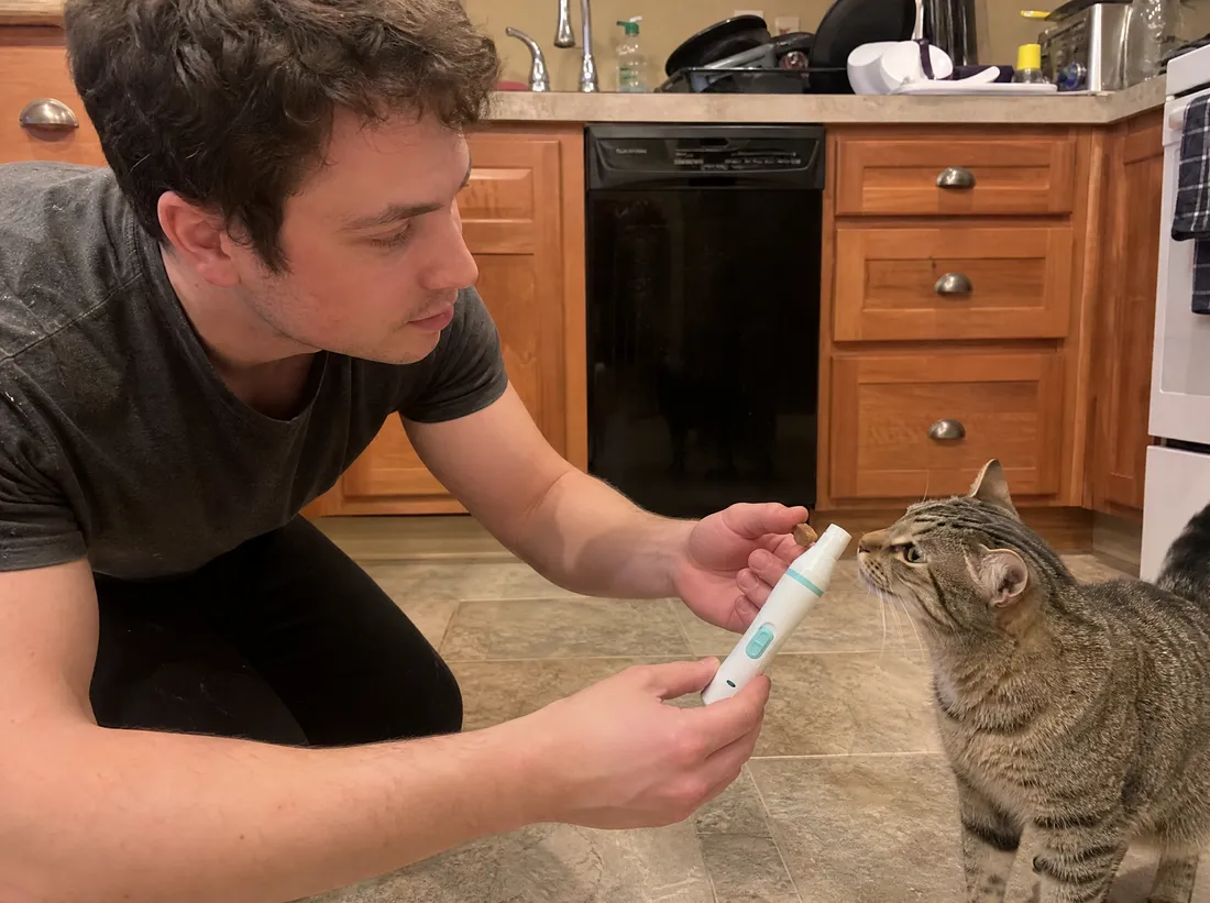 Man letting a tabby cat sniff the Pawzaw grinder while offering a treat